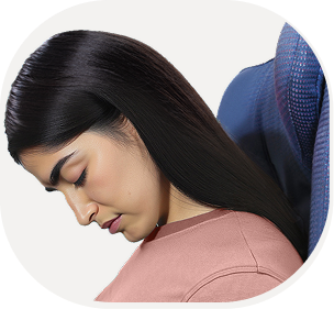 Woman with long dark hair sitting in an airplane seat, looking uncomfortable without a neck pillow